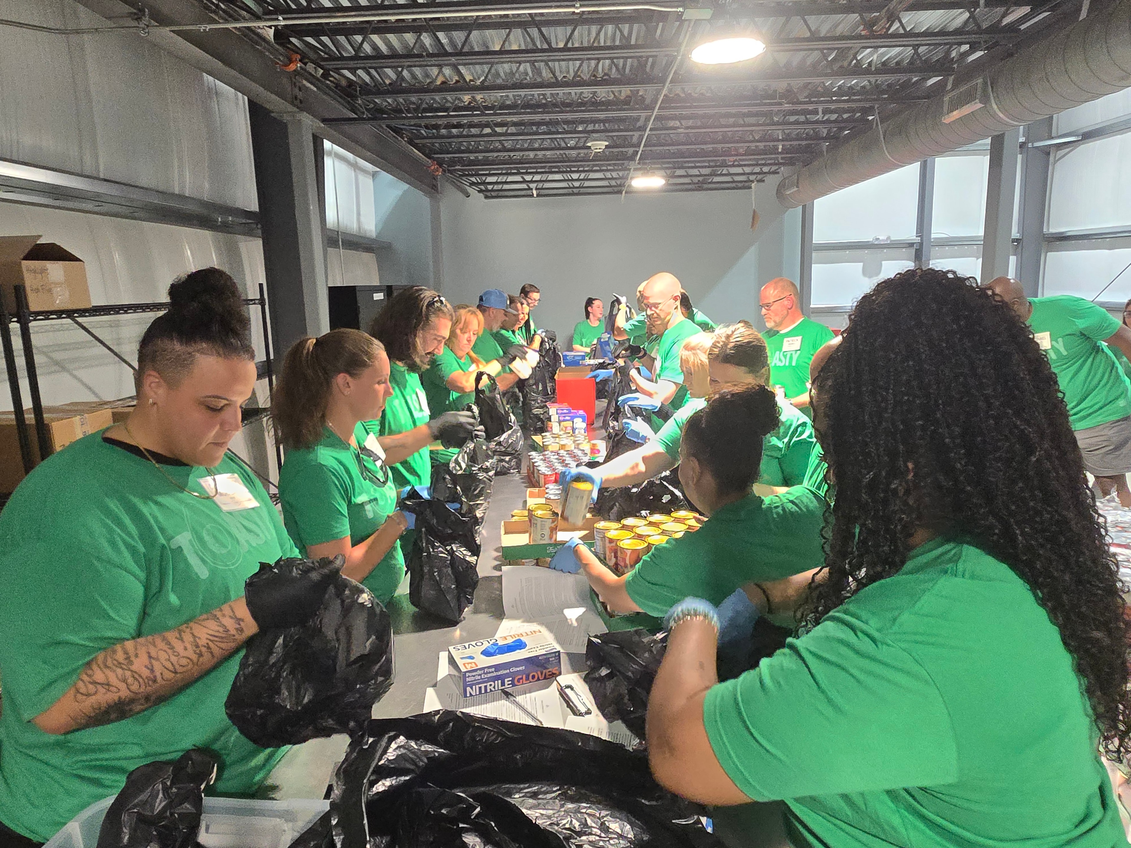 Volunteers in green shirts packing food at a Food Bank of Manatee packing event